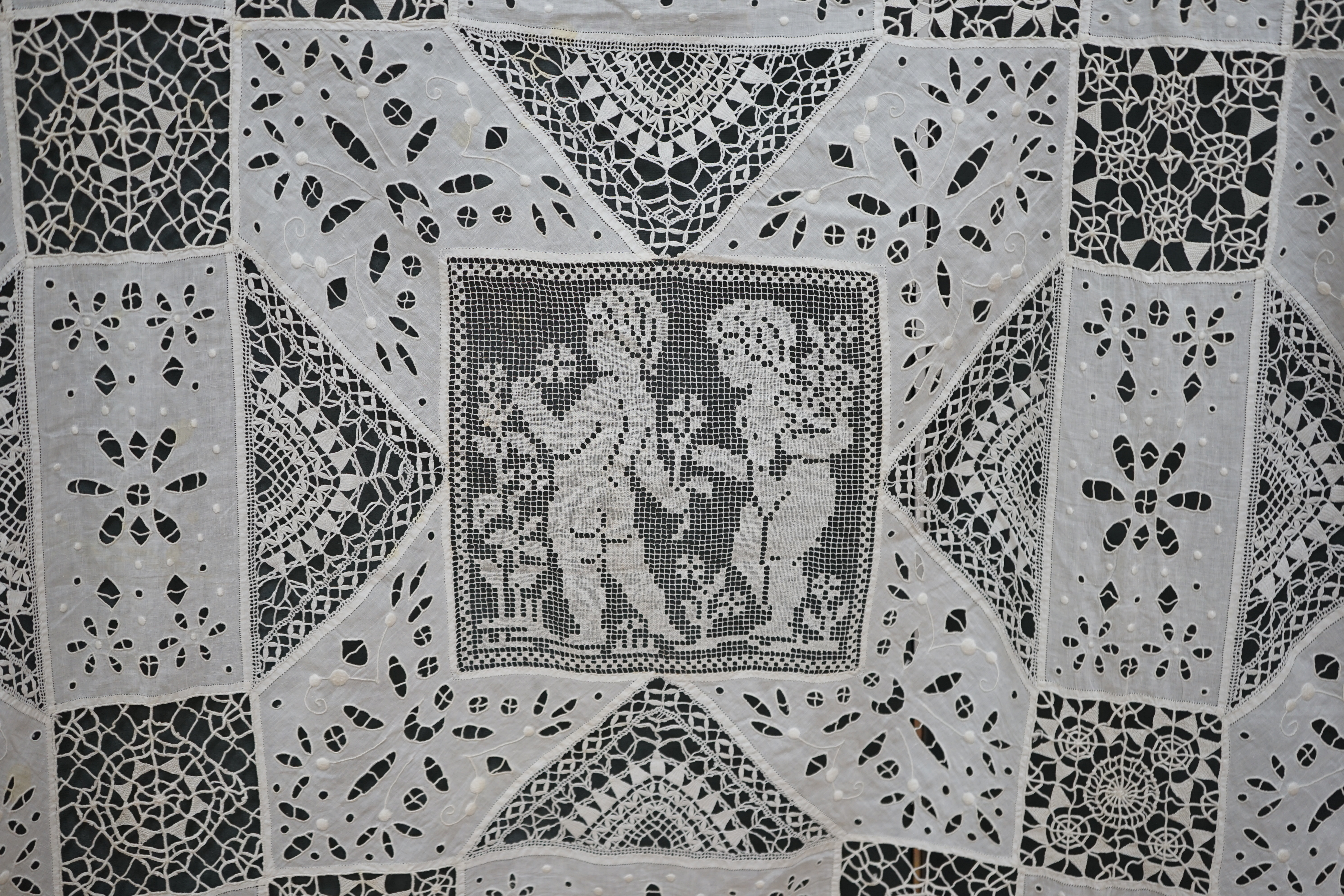 An early 20th century Italian bedcover, worked with fillet lace insertions of putti, white multi patterned fine linen cut work squares and similar multi patterned hand needle lace insertions, creating a unique and totall